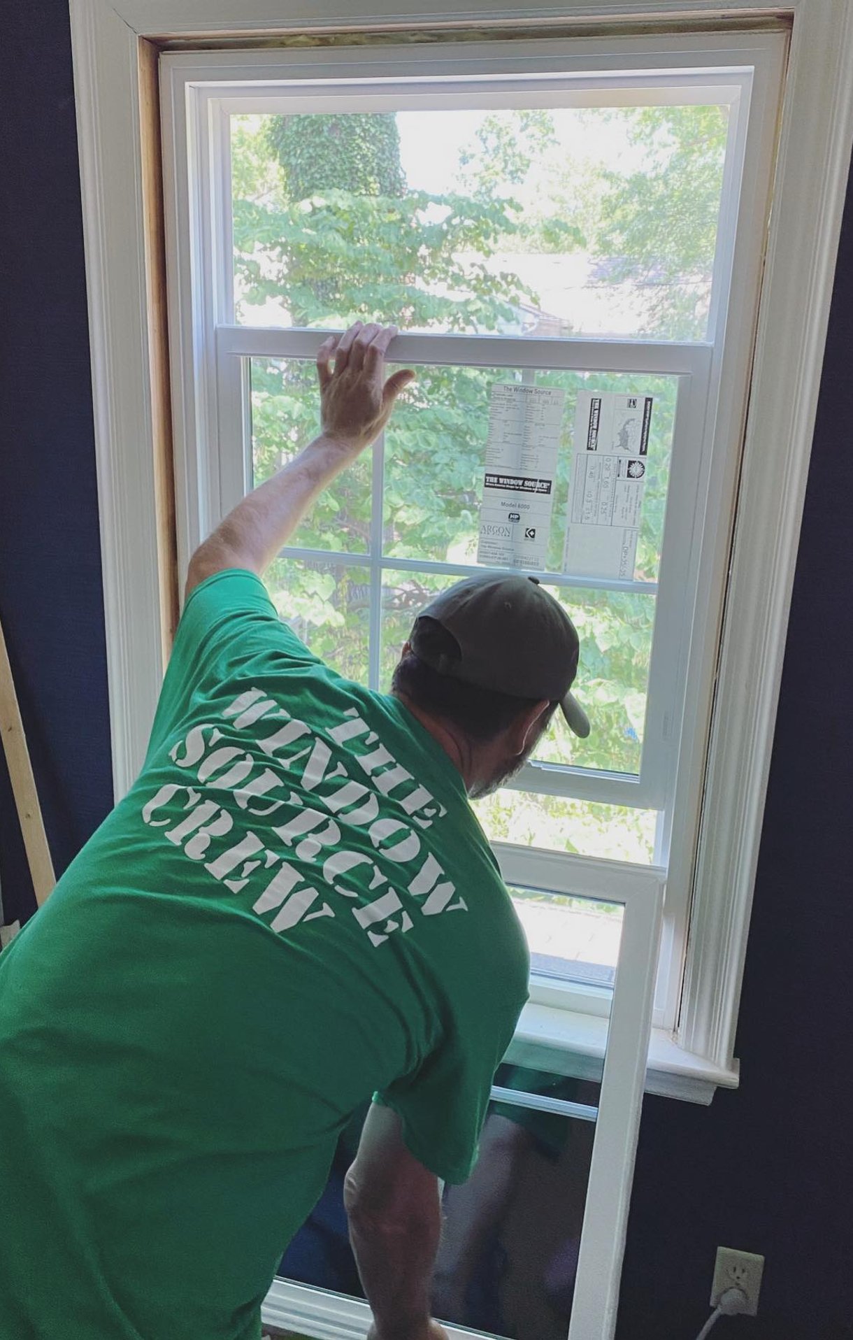 Wooden front door with glass panels, white siding, greenery.